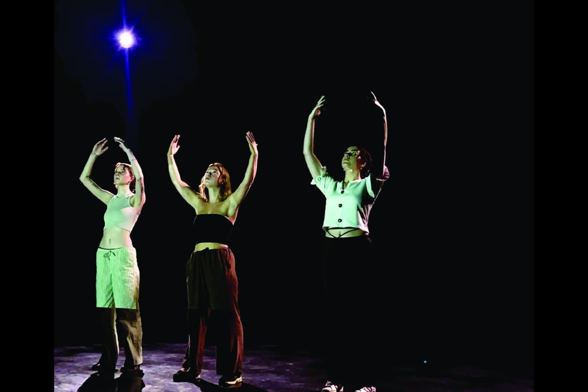 Three performers reaching upward under a single blue spotlight on a dark stage